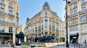 Immeuble de standing de style haussmannien à l'angle de la rue Réaumur et de la rue des Petits Carreaux à Paris 2e, baigné par le soleil d'été avec des passants en tenue estivale.