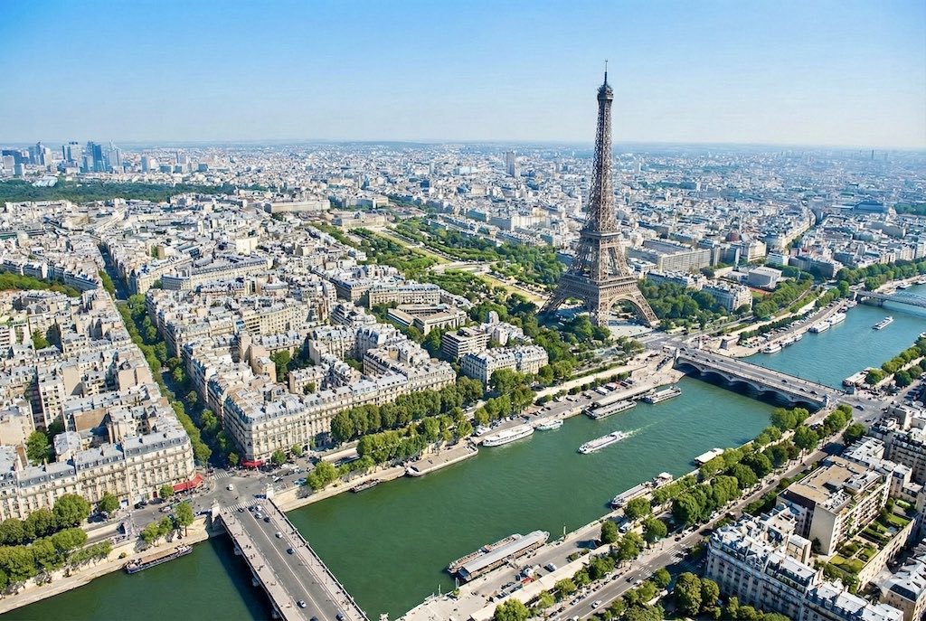 Vue aérienne panoramique de Paris avec la Tour Eiffel et la Seine, illustrant l'estimation immobilière d'appartements haussmanniens de prestige.